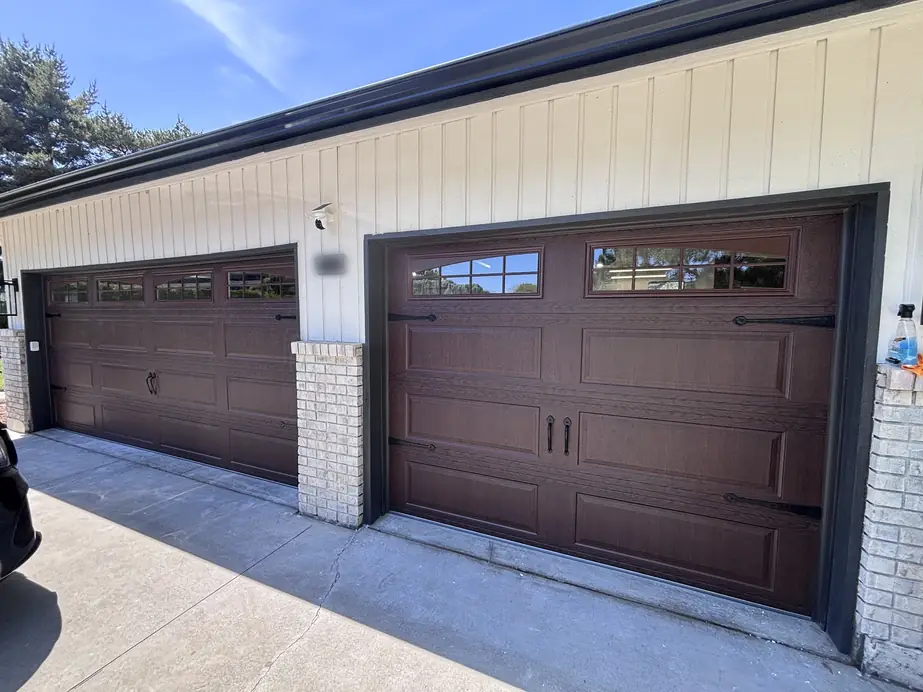 Two dark brown carriage-style garage doors with arched window tops and black strap hinges, installed by Masters Garage Doors