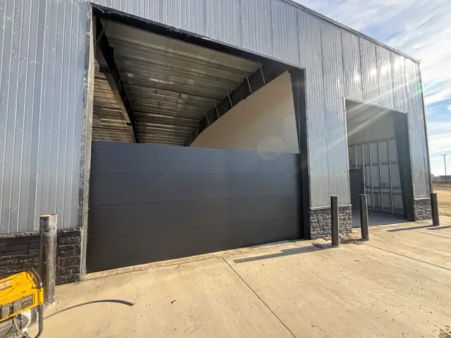 Black insulated sectional door being installed in a metal commercial building