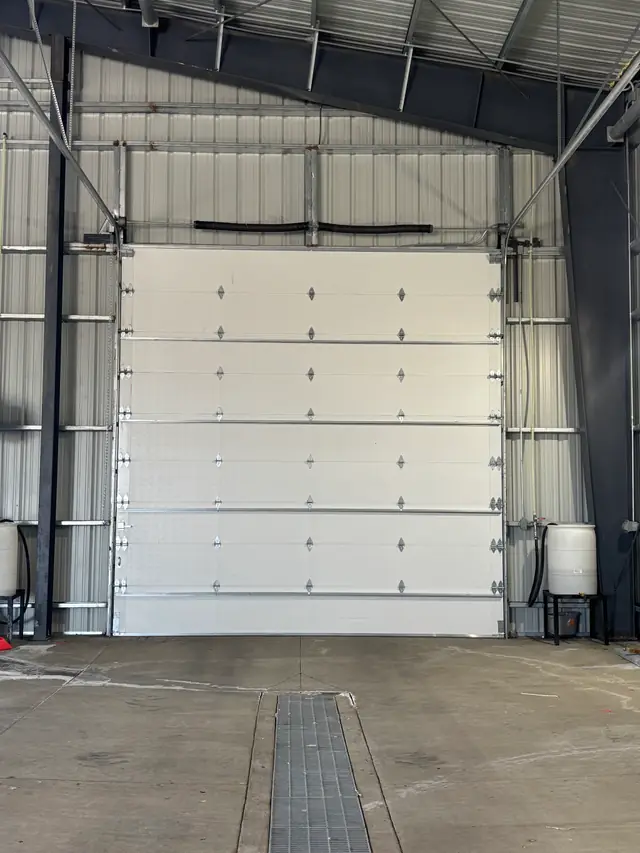 Tall white commercial sectional door seen from inside a steel building