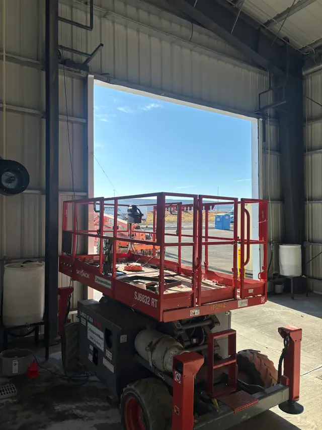 Red scissor lift parked in an open bay of a steel building during a door job