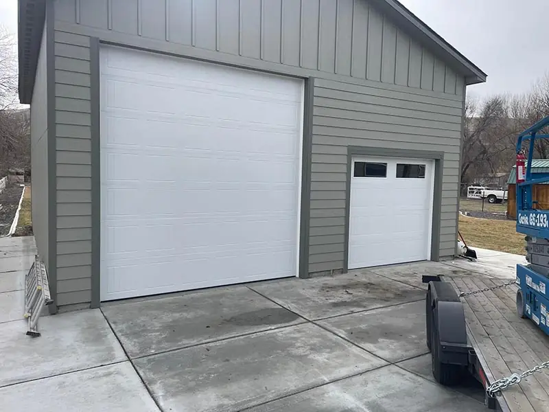 Tall white shop door beside a standard door on a grey board-and-batten building