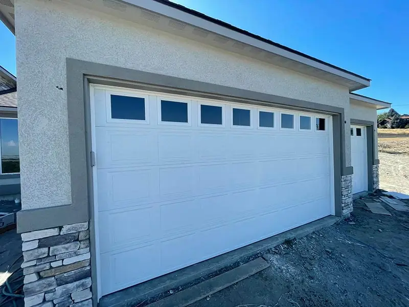 Wide white garage door with a long row of windows on a new stucco house