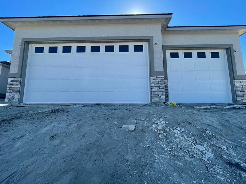 Two white garage doors with window tops between stone pillars on a new build