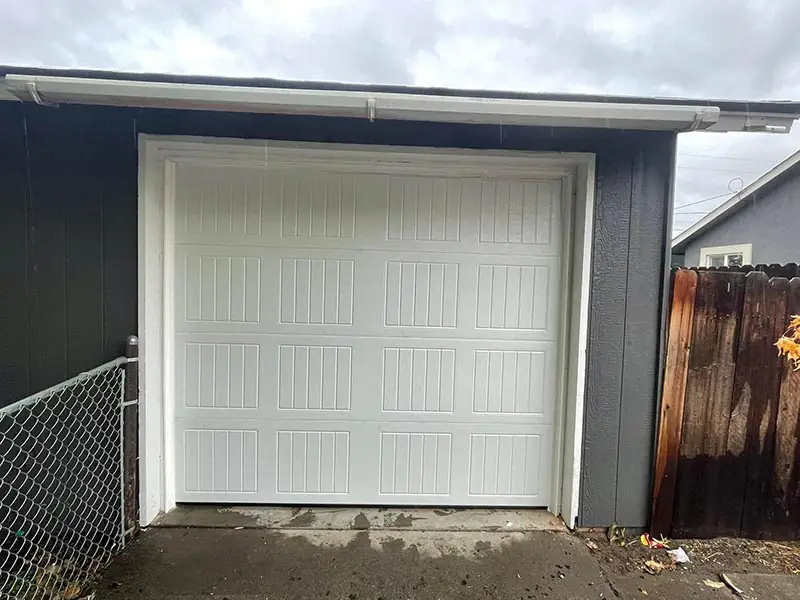 Single white ribbed garage door on a dark grey outbuilding