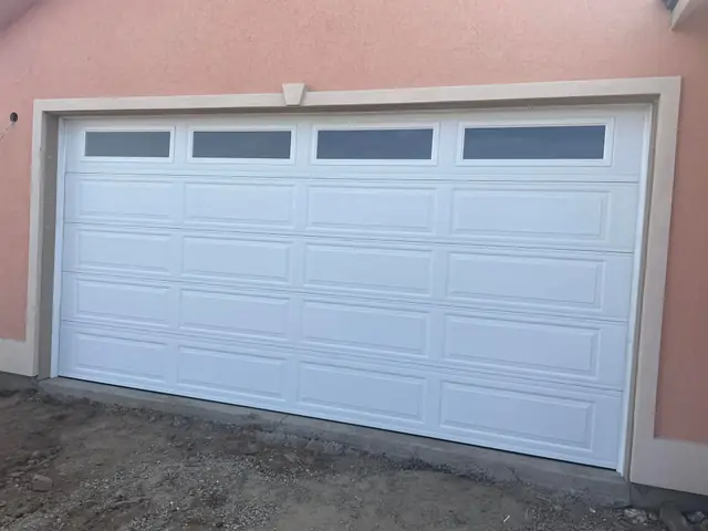 Finished white long-panel garage door with a row of windows on a peach stucco house