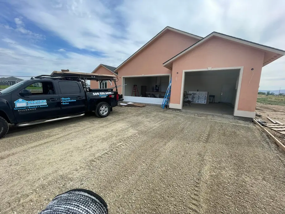 The black Masters Garage Doors pickup, lettered with the phone number and Licensed, Bonded, Insured, parked at a new-build job