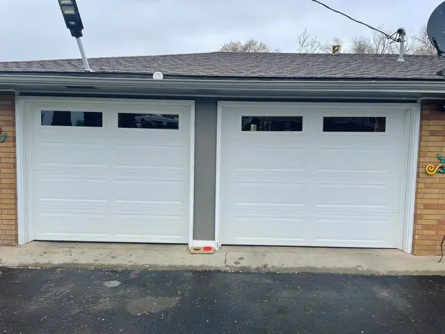 New white garage doors after a repair and replacement on a brick house