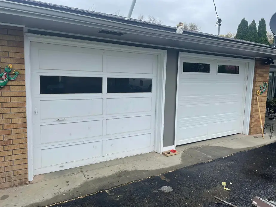 An old white garage door beside a newly installed door on a brick house